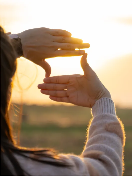 Pige har hænder op foran solnedgang